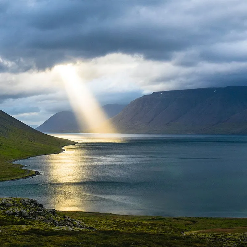 Sunlight breaking through clouds over a mountain lake